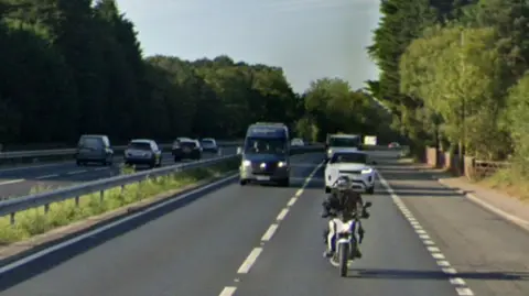 Google Google Maps screen grab from one side of the A12. Looking directly at traffic coming towards it with a white and blue motorbike in foreground and Range Rover and VW van in the background. 
To the left in the background, traffic can be seen going in the opposite direction. 