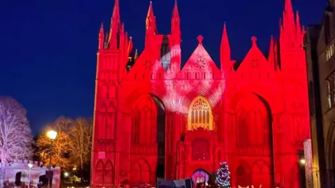 We Love Peterborough The West Front of Peterborough Cathedral lit up in red at night.