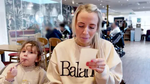 Bianca Osborne looks at a receipt while she sits in Costa with four-year-old daughter Amelia