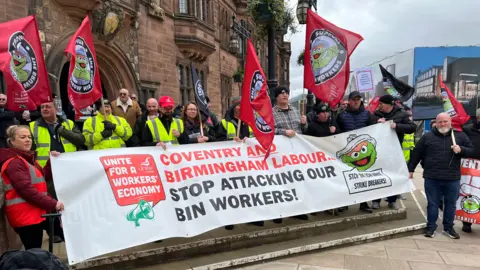 Protestors outside Coventry Council House wave red flags which read "support the Brum bin workers". A large sign held up at the front reads "Coventry and Birmingham Labour stop attacking our bin workers"