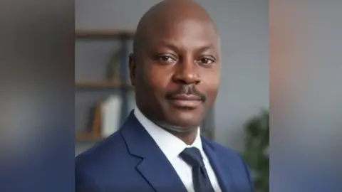 Ark Training Social Care Consultancy Ltd Winston is wearing a a blue suit and and white shirt and is slightly smiling at the camera in this head and shoulders shot.