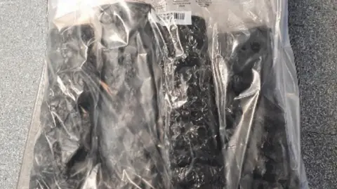 National Crime Agency Four vacuum-sealed black bags, that are long and cylindrical, placed inside clear plastic evidence bags