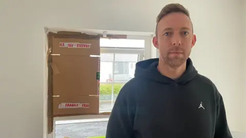 Martin Caskey stands inside his home with cardboard over the windows