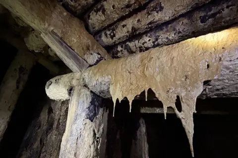 Lucy Dusgate Cream coloured semi-translucent film hangs from a horizontal wooden beam