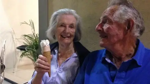 Jocelyn and Mark Tress sits next to each other as she holds the camera ice cream. He looks out of the camera.