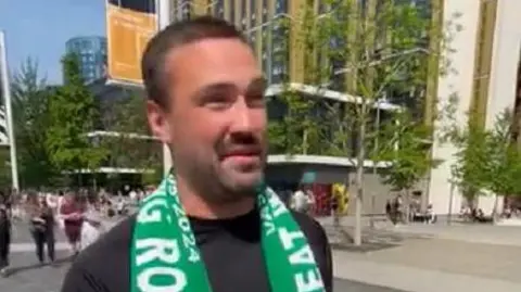 PA Media Man with short dark hair and beard wearing a green Wakering scarf