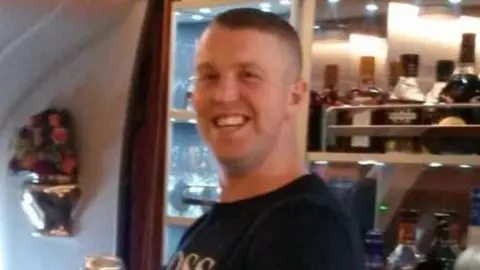 Family handout A man with short hair is smiling and looking toward the camera. He is wearing a short sleeve black t-shirt.