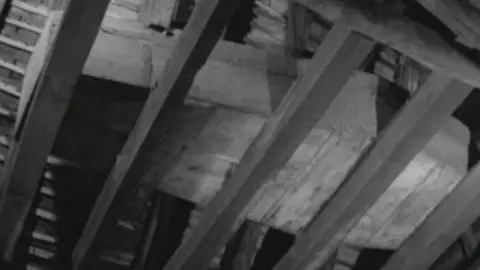 A wooden coffin in the rafters of a building, supported by wooden beams.  