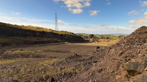 A quarry on sunny day. A electricity pylon is in the distance.