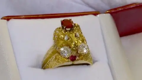 A golden ring in the shape of a ram with diamonds for eyes sits in a cushioned box.