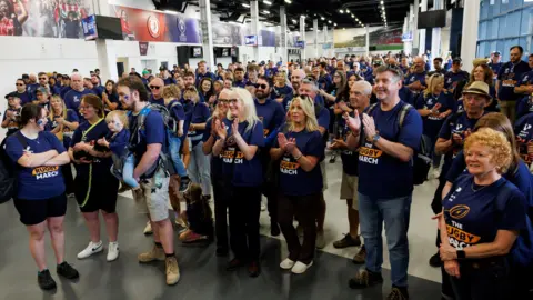 Bristol Bears/Ashton Gate People with the Bristol Bears Foundation in navy the Rugby March t shirts. There are a few hundred people in the picture all looking forward and smiling, with many clapping their hands. 
