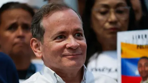 Getty Images Juan Pablo Guanipa, who has greying hair and wears a white shirt, smiles as he is pictured outside following his release from prison in Caracas 