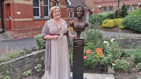 East Hampshire District Council Jane Austen’s Great Niece, Caroline Knight, standing by the statue during the unveiling celebrations. She is looking away from the camera. Her right hand is touching the sculpture.