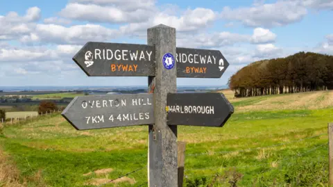 Getty Images A wooden sign which says 'Ridgeway Byway' and points to Marlborough and Overton Hill. In the background are grass and trees, and some rolling hills and fields in the distance.