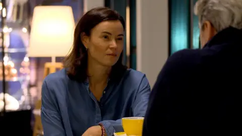 Malena Abelsen is sitting at a table, wearing a blue shirt, with a yellow cup in front of her