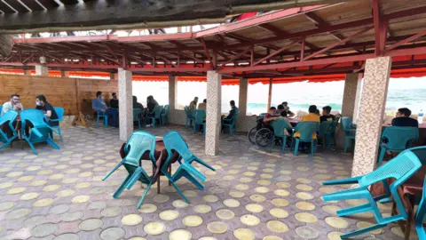 Google A photo taken before the war shows people sitting at tables overlooking the sea in the cafe. They are sat in blue plastic chairs. Not all tables are occupied.