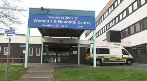 A infirmary  entranceway  with a motion   to the neonatal ward. An ambulance is parked outside