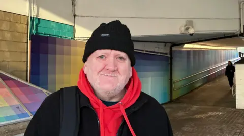 Steve Jones/BBC Keith Robinson, who is wearing a black beanie hat and a red sweater.