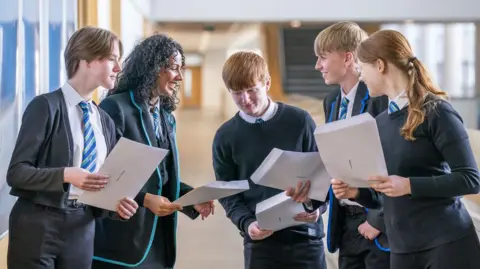 PA Media Students in uniforms gathered in a school corridor holding their exam results