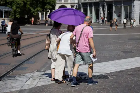 Elderly people with an umbrella used to protect themselves from the sun are walking through the streets of Grenoble. France, Isere, July 2, 2026. Illustrative image of the city of Grenoble during a heatwave.