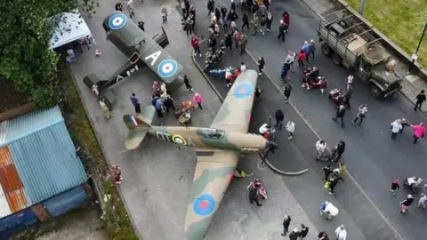 Rochdale Council Overhead drone view of two wartime plane replicas as people gather around to look at them. An old military vehicle appears on the side.