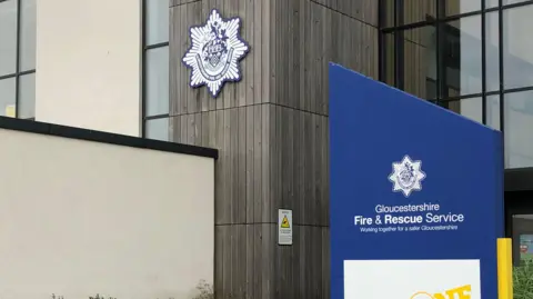 Wood, glass and metal fronted building with a blue sign outside that reads Gloucestershire Fire & Rescue Service