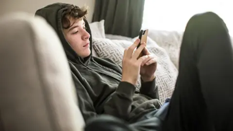 Getty Teenage boy wearing a hoodie lying down and looking at his phone