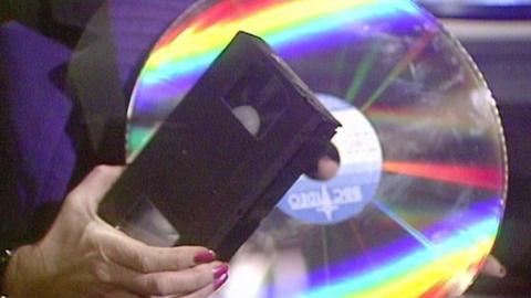Woman holding a VHS tape and a laser disc.