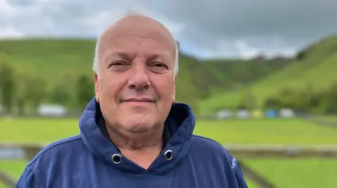 A man stood in front of green fields and hills