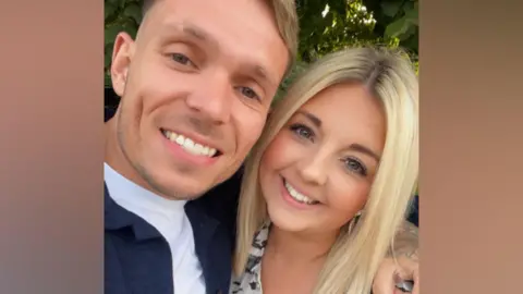 A blond man wearing a blue jacket and white shirt. He is standing next to a blonde woman in a black and white shirt. 