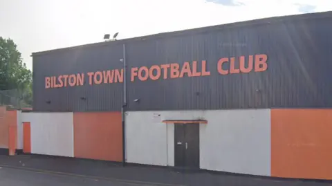 Google The club's orange and black or grey insignia is on the outside of a long, square building next to a main road with the name of the club in orange letters on the top exterior.