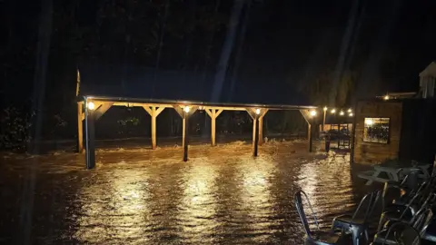 Mark Bentham A wooden structure is half under water with garden chairs and tables stacked to one side.