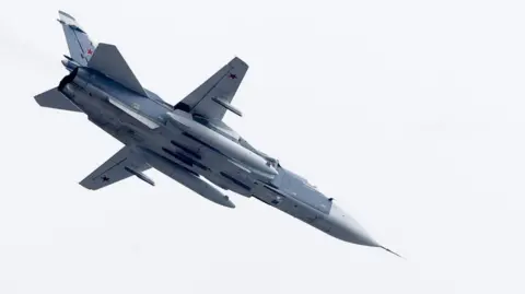 Photo of a Russian air force Su-24 fighter jet airborne against a clear blue sky.