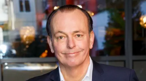 Getty Images Quentin Willson in 2017 - smiling and dressed in a dark blazer, and white shirt