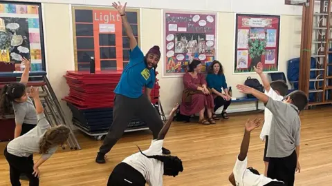 BBC Six children dancing along with a smiling teacher showing them which moves to do