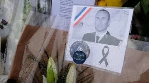 AFP A photo of gendarme Arnaud Beltrame attached to a bouquet in Carcassonne in southwest France on 25 March 2018