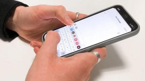 Hands hold a mobile phone, the person is wearing silver rings and has opened a new message tab on the screen of the device.
