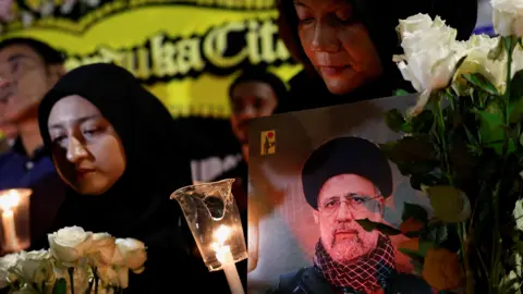 A woman holding a picture of the late Iranian President Ebrahim Raisi, attends a vigil to pay tribute to him and other victims who died in a helicopter crash, outside the Iranian embassy in Jakarta, Indonesia
