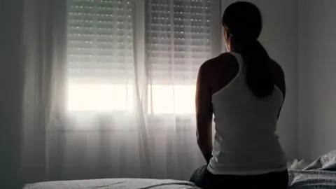 Alvaro Medina Jurado A pistillate   sits connected  a furniture  with her backmost  to the camera, looking towards a window