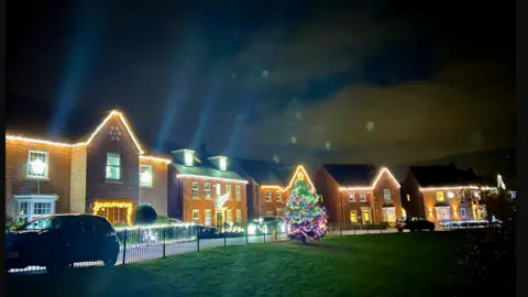 LDRS Tree with lights on in front of a row of detached houses, which have lights on