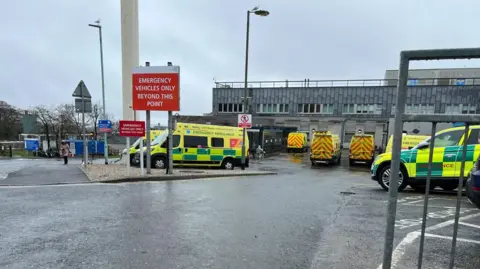 Ambulances parked outside Derriford Hospital in Plymouth on a rainy day.