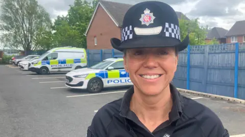 Photograph of Chief Superintendent Clare Jenkins from Greater Manchester Police. The image shows police vehicles in a car park.