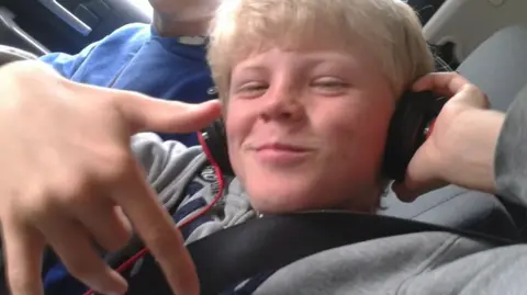 Harris Trust A boy in a grey sweater, wearing headphones, smiling at the camera