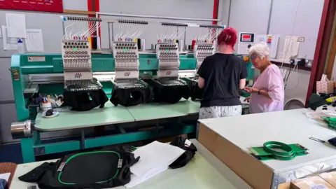 Two women are chatting next to some branding machinery