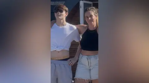 A teenage boy stood with a woman who has her arm around him.