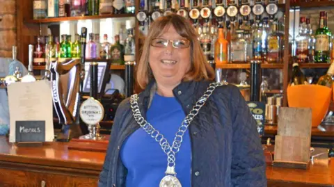 Tetbury Town Council Ann Pearce in her mayoral chain standing in a pub