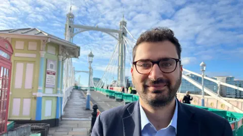 A man in a blue shirt stands in front of a closed bridge