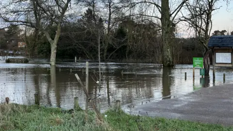 Julia Gregory/BBC A river seeps onto a pathway and grassy verge.