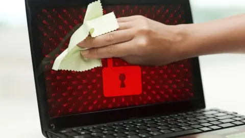 Getty Images A composite image shows someone cleaning a laptop screen while a red padlock image is displayed on screen