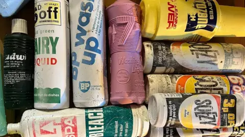 Sanday Community Craft Hub Ten differently branded plastic bottles retrieved from the beach in Sanday lie alongside one another. Some are emblazoned with a "Sqezy" logo, a brand which has not been manufactured since the 1980s.